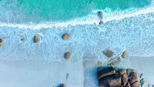 Faszinierende Drohnenaufnahme vom Plage de Boutrouilles: T&uuml;rkisblaues Wasser und wei&szlig;er Gischt-Schaum treffen auf hellen Sandstrand und markante, dunkle Granitfelsen.
