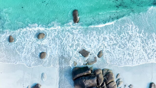 Faszinierende Drohnenaufnahme vom Plage de Boutrouilles: T&uuml;rkisblaues Wasser und wei&szlig;er Gischt-Schaum treffen auf hellen Sandstrand und markante, dunkle Granitfelsen.