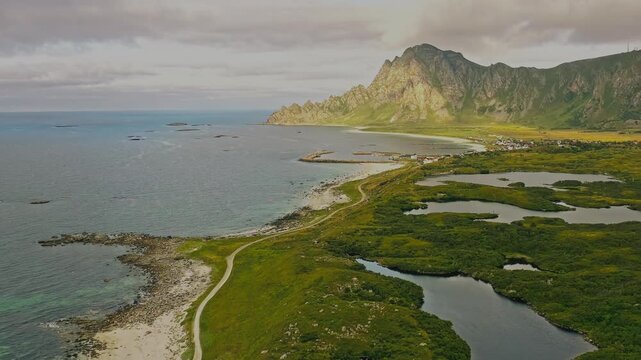 A breathtaking cinematic drone shot of Norway's rugged coastline, with the deep blue sea stretching endlessly on one side and dramatic landforms on the other. The aerial perspective follows the shorel