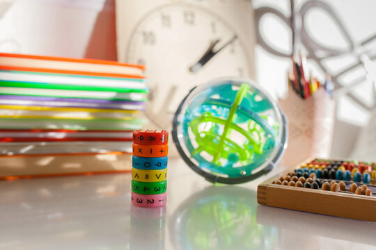 Colorful educational math game cylinder on desk with books, globe maze puzzle and abacus. Back-to-school concept, STEM learning and development, classroom study and fun mathematics for children.