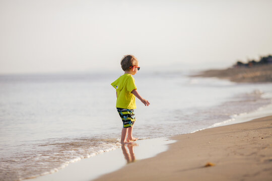 Little toddler boy playing on beach during sunset.Childhood, summer holidays, freedom, and joy of simple outdoor activities. Safety of children by water.