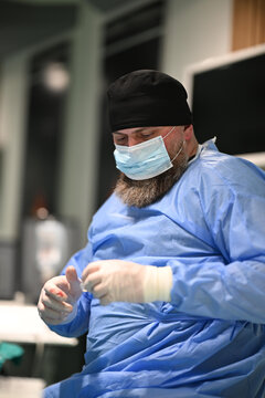 Bearded Surgeon in Surgical Gown and Mask Preparing Gloves in Operating Room Environment