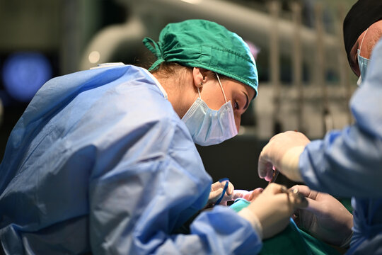 Female Surgeon and Team Performing Delicate Surgery in Modern Operating Room Wearing Masks and Scrubs
