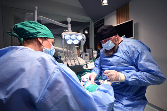 Dental Surgery Team Performing Oral Procedure On Patient In Modern Dental Clinic With Surgical Lights