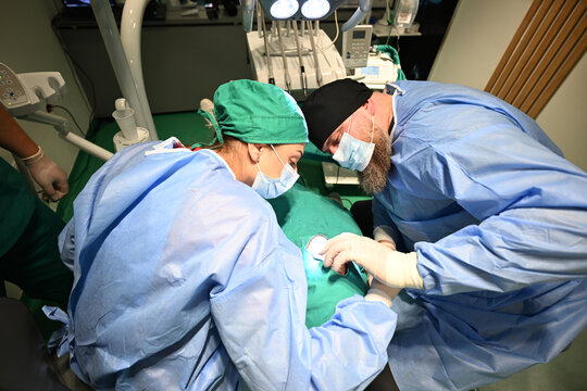 Dental Surgeons Performing Oral Surgery on Patient in Sterile Clinic With Surgical Light and Equipment