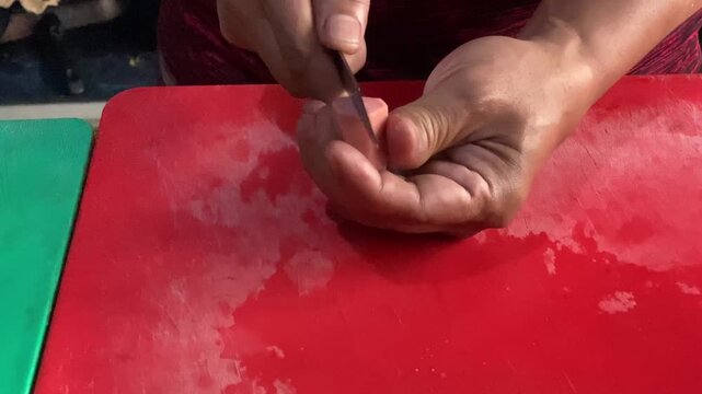 Hands slicing raw sausages on a cutting board A descriptive close-up stock footage clip showing a person's hands using a sharp kitchen knife to slice raw sausages into pieces on a cutting board. 