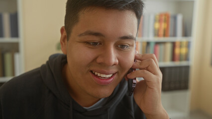 Man holding smartphone to ear and smiling toward monitor in an office building while seated at desk  friendly conversation. © Krakenimages.com