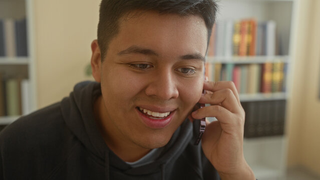 Man holding smartphone to ear and smiling toward monitor in an office building while seated at desk; friendly conversation.