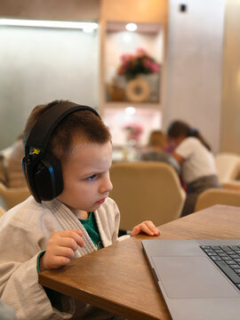 Focused Young Boy Wearing Headphones Using Laptop in Cozy Cafe During Online Learning Session