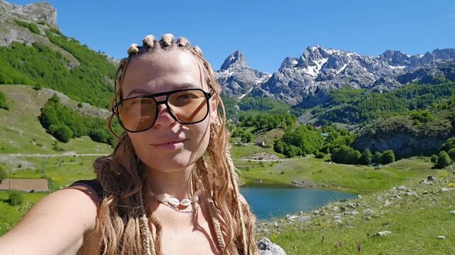 Young woman with braided hair and sunglasses filming selfie video with Bukumirsko Lake and snowy mountains in Montenegro