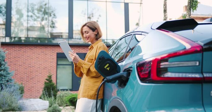 Young woman charging electric car while using tablet outdoors