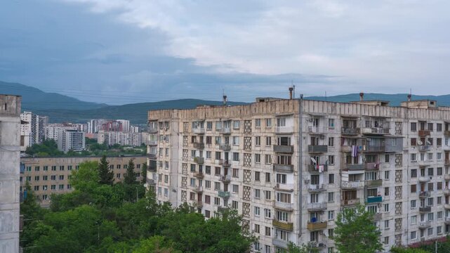 Time-lapse video overlooking old blocky Soviet-era apartment buildings in Tbilisi, Georgia, capturing the transition from evening sunlight to dark storm clouds, heavy rain, and lighting up windows