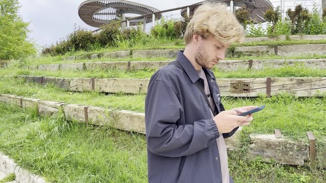 Lifestyle portrait of young man using a smartphone outdoors.Man  type message on smartphone in summer  city park. 