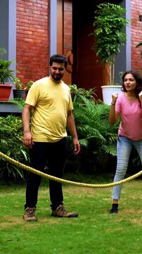 Indian kids playing tug of war or rassi khech in home garden while parents cheer them, spending quality fun time together enjoying traditional outdoor sports bonding during weekend family activity