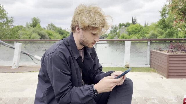Lifestyle portrait of young man using a smartphone outdoors.Man  type message on smartphone in summer  city park. 