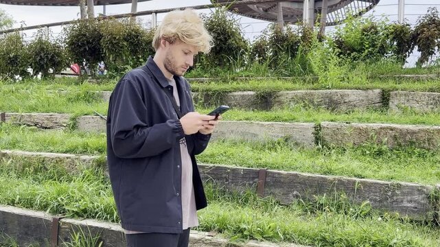 Lifestyle portrait of young man using a smartphone outdoors.Man  type message on smartphone in summer  city park. 