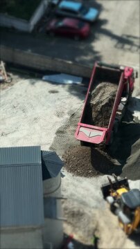 Top view of a red dump truck unloading a pile of gravel and dirt next to a backhoe loader at a construction site