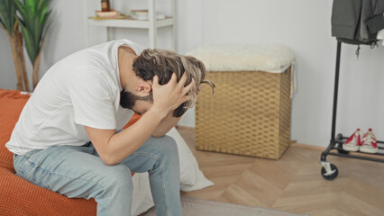 Fototapeta premium Man sitting on bed holding neck and head, clutching head with hands for headache in a building bedroom; anxiety stress fatigue.