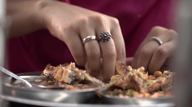 Human hand breaking soft flatbread during dining experience in India.