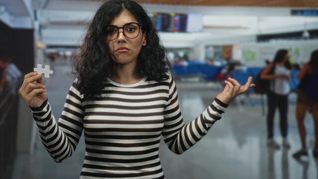 Woman holding a puzzle piece and pointing finger to chest in an airport terminal, striped shirt visible; confusion uncertainty travel stress.