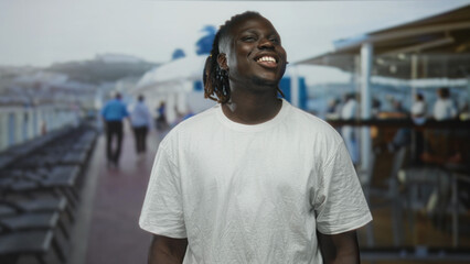 Fototapeta premium Man smiling with face tilted back on cruise deck near ship rail, wearing white t shirt and dreadlocks, outdoors and relaxed; joy relaxation travel.