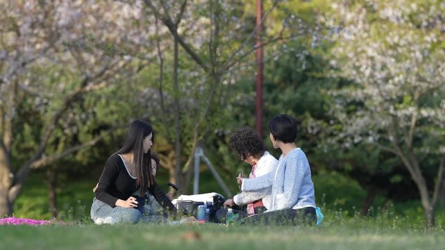 Soft spring light bathes blooming cherry trees. Family gathers on green grass, sharing quiet moments. Mother holds child close, father smiles gently beside her. Natural beauty frames tender