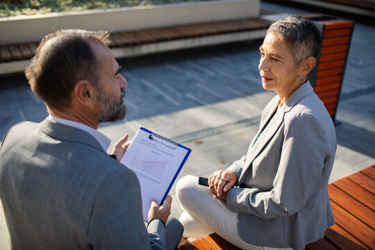 Two business professionals reviewing a report outdoors on a bench