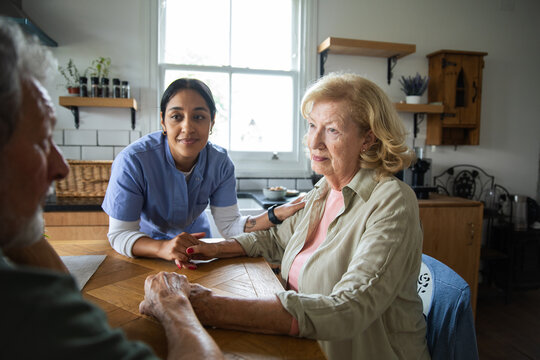 Nurse caregiver comforting senior couple in home kitchen