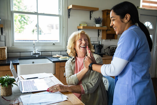 Senior woman and caregiver high-fiving at home kitchen table