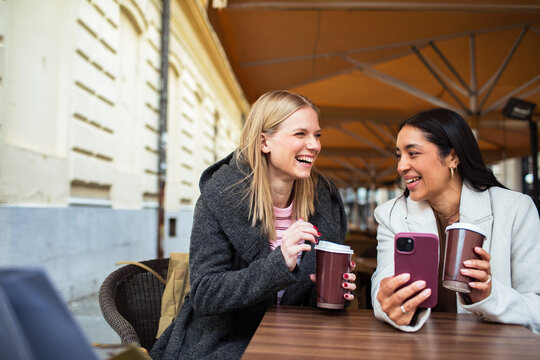 Two friends sharing coffee and laughs at a city sidewalk cafe