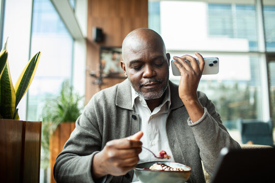 Mature man on phone while eating dessert in modern cafe