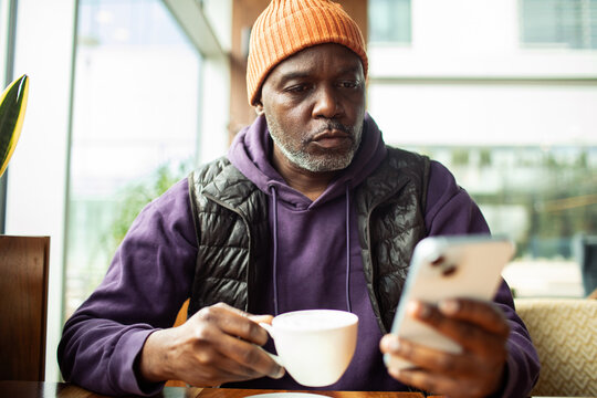 Middle-aged man drinking coffee and using smartphone at cafe