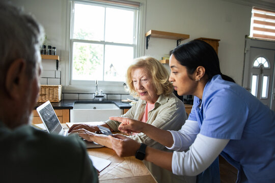 Caregiver assisting senior couple with online banking at home