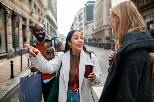 Three friends chatting and pointing on a city street while shopping