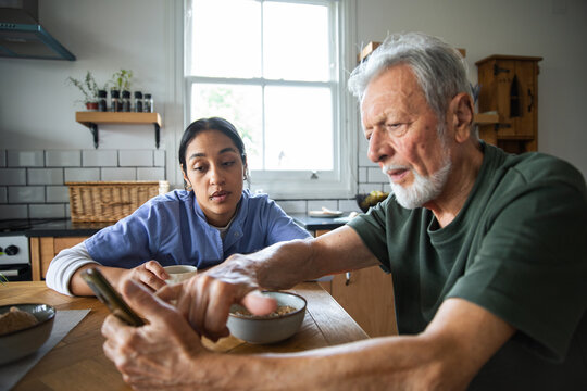 Caregiver helping senior man with smartphone at kitchen table