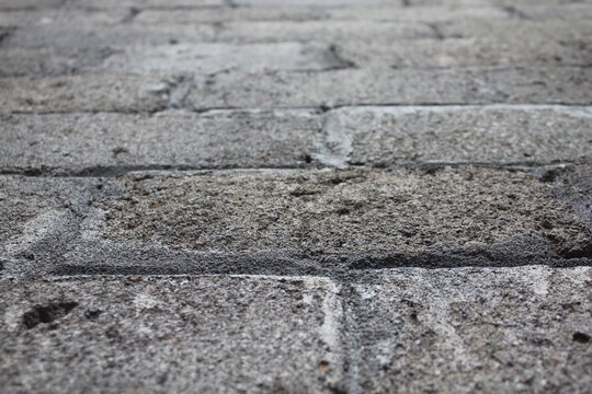 Close-up of textured gray brick pavement with shallow depth of field. Ideal urban background, construction texture, stone walkway surface, and architectural design concept.