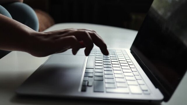Close-up of hands typing on a laptop keyboard in soft, moody lighting