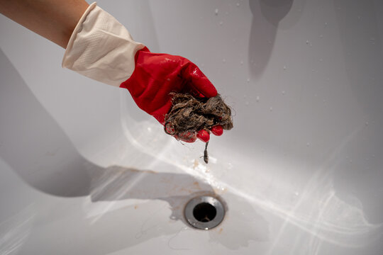 Close up of gloved hand holding tangled hair removed from blocked shower drain. Concept of bathroom cleaning, household maintenance, plumbing problems and regular drain care to prevent water blockage.