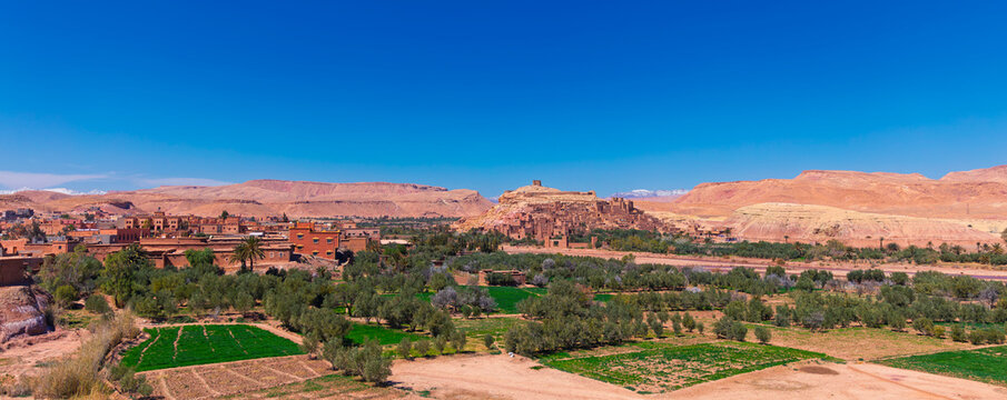 Panoramic view of ait ben haddou kasbah with green oasis and snowy mountains in morocco