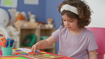 Obraz premium Girl placing green wooden puzzle piece with hand on red activity table in a playroom inside a building; concentration play.