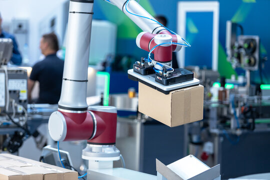 Collaborative robotic arm handling a cardboard box in an automated factory, illustrating warehouse automation, smart logistics, material handling, robotics, and Industry 4.0.