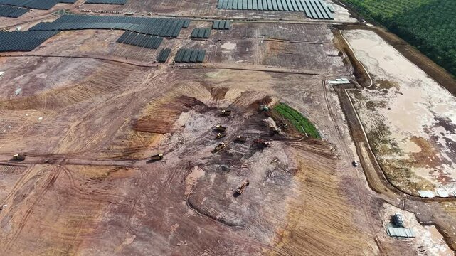 Aerial drone view of solar farm construction with excavators, trucks and mounting panel arrays.