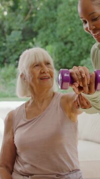 Vertical video: Placing dumbbell PT holding wrist guiding senior raising arm for rehab on patio