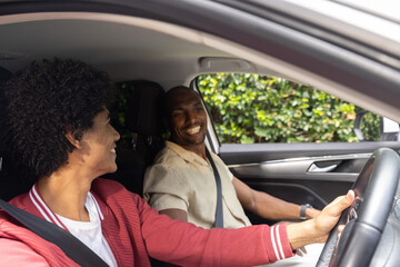 Fototapeta premium Couple African American man holding wheel driving and woman leaning both belted in parked car