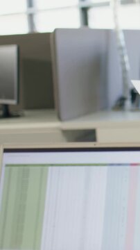 Vertical video: Typing dark-cuff hand on laptop keys checking sheet at cubicle using paper chart