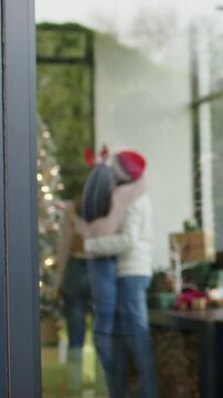 Vertical video: Embracing couple pointing up at tree, swaying at home celebrating in festive hats