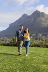 Obraz premium Couple walking together across grassy lawn at base of mountain, wearing sneakers and headband