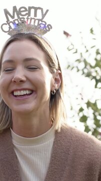Vertical video: Camera pan woman laughing, adjusting Xmas headband in cardigan in yard, copy space