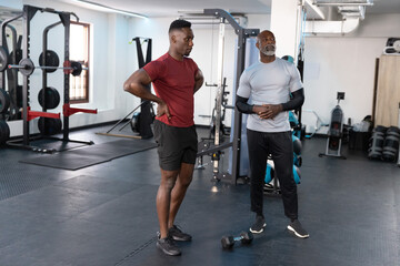 Fototapeta premium African American trainer coaching senior trainee at gym in maroon shirt gray top near hex dumbbell