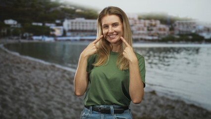 Fototapeta premium Blonde woman pulls t shirt collar with both hands while smiling and tilting head at a seaside beach resort; serenity.